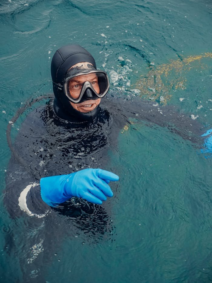 Services An adult diver in a wetsuit with gloves pointing while swimming in clear ocean water.
